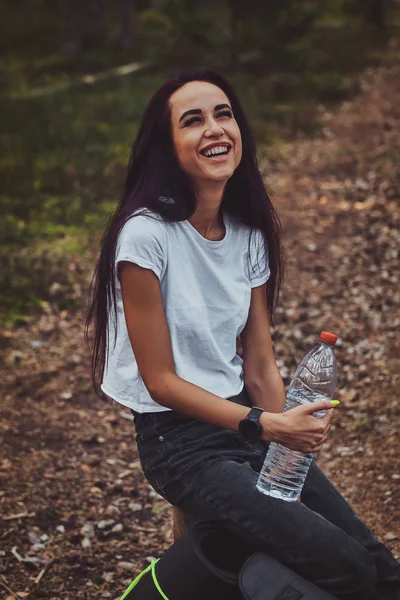 Ung kvinna vilar i skogen medan du håller flaska vatten. — Stockfoto