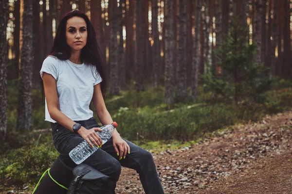 Mujer joven está descansando en el bosque mientras sostiene la botella de agua . — Foto de Stock