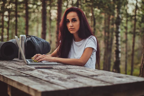 Estudante alegre está trabalhando no laptop no meio da floresta . — Fotografia de Stock