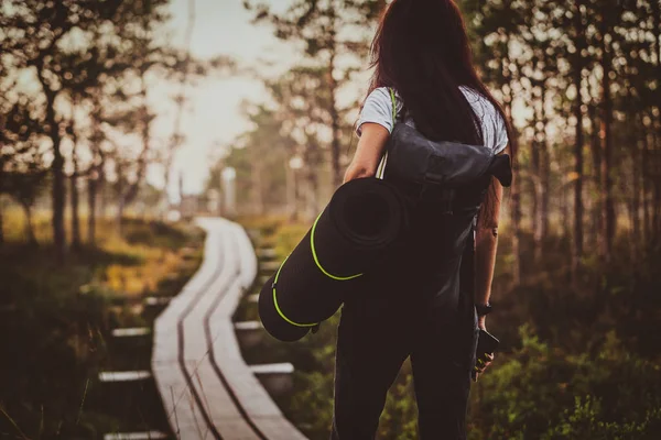 Flaca mujer es senderismo por el camino de madera en el medio de exuberante bosque de pinos . — Foto de Stock