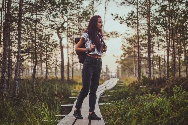 Flaca mujer es senderismo por el camino de madera en el medio de exuberante bosque de pinos . — Foto de Stock