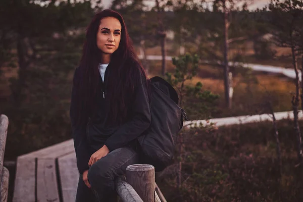 Young student is checking time on her watch while leaning on the guardrail in the middle of the forest.