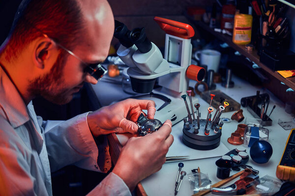 Serious watchmaker  is repairing cutomers order at his own repairing studio