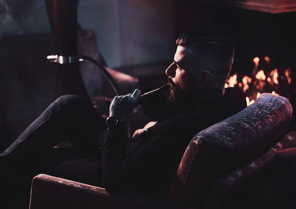 Hombre barbudo guapo es relajarse en el salón mientras fuma narguile —  Fotos de Stock