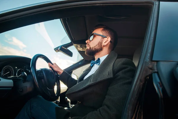 Hombre moderno arreglado en gafas de sol está sentado en su coche en el aparcamiento . — Foto de Stock