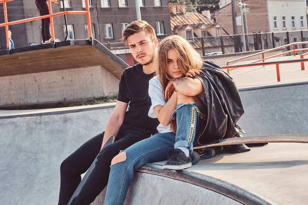 Joven pareja atractiva de estudiantes están sentados en skatepark con sus longboards —  Fotos de Stock