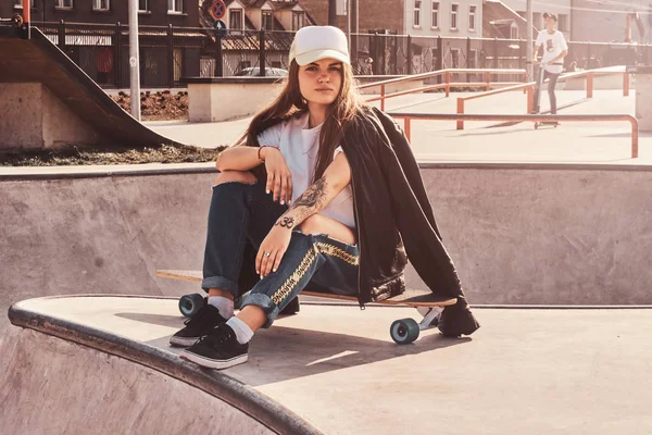 Молода виснажлива дівчина сидить на своєму дошці в скейтпарку — стокове фото