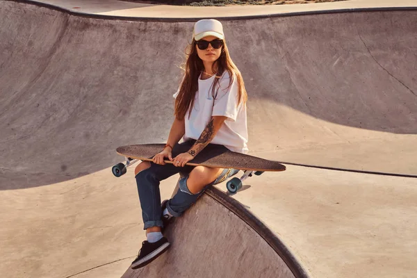 Bella giovane donna in occhiali da sole e cappuccio è seduto allo skatepark — Foto Stock