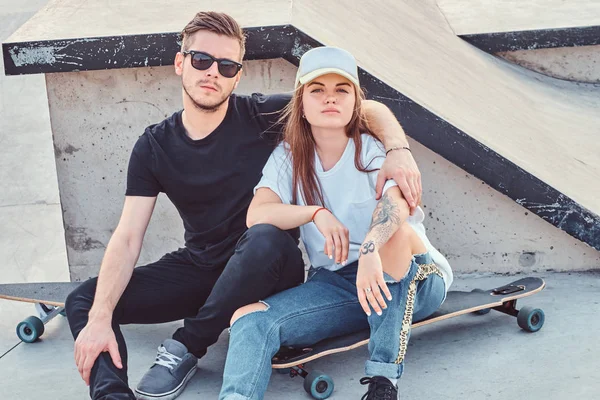 Молодая модная пара сидит в солнечном скейтпарке с длинными досками — стоковое фото