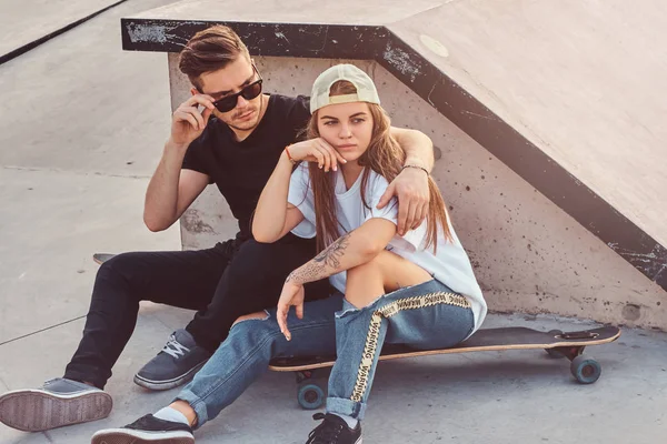 Młoda modna para siedzi w słonecznym skateparku ze swoimi longboardami — Zdjęcie stockowe