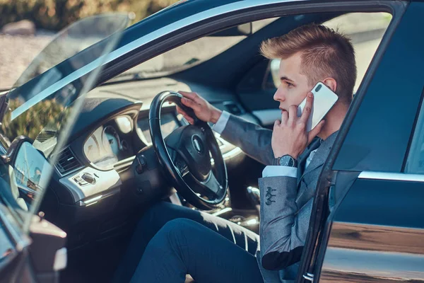 Jovem empresário está sentado em seu carro no estacionamento enquanto conversa por telefone celular . — Fotografia de Stock