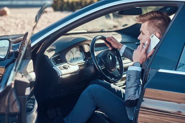 Jovem empresário está sentado em seu carro no estacionamento enquanto conversa por telefone celular . — Fotografia de Stock