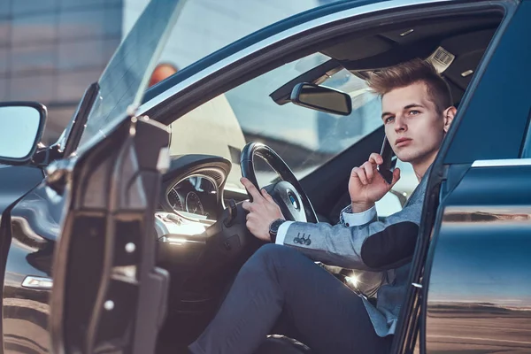 Young businessman is sitting in his car at the parking while talking by mobile phone. — Stock Photo, Image