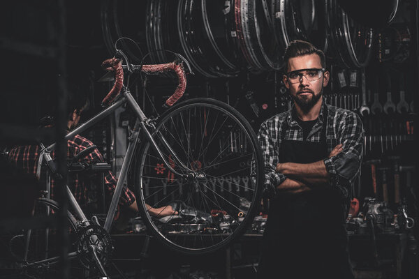 Handsome man in glasses is standing near fixed bicycle at his own workshop.
