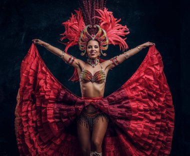 Kırmızı tüy kostümlü yetenekli neşeli dansçı küçük karanlık stüdyoda poz veriyor.