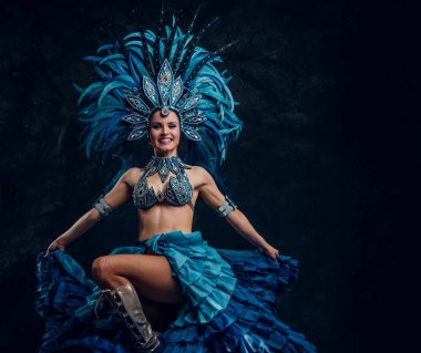 Kırmızı tüy kostümlü yetenekli neşeli dansçı küçük karanlık stüdyoda poz veriyor.