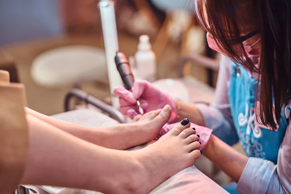 Joven maestro de uñas alegre está trabajando en los clientes uñas de los pies en su estudio de pedicura . —  Fotos de Stock