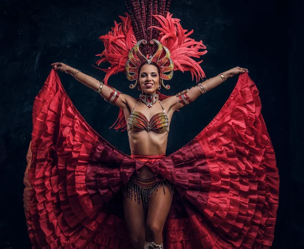 Begabte fröhliche Tänzerin im roten Federkostüm posiert im kleinen dunklen Studio. — Stockfoto