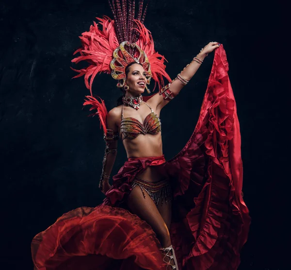 Talented joyful dancer in red feather costume is posing at small dark studio. — Stock Photo, Image