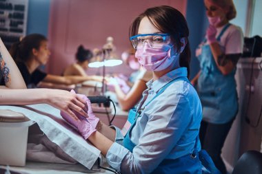 Genç manikür ustası işyerinde kadın tırnakları üzerinde çalışıyor..