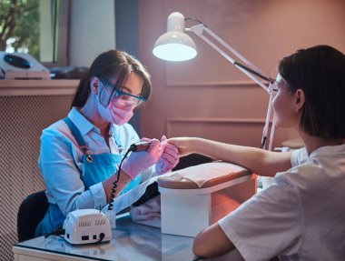 Genç manikür ustası işyerinde kadın tırnakları üzerinde çalışıyor..