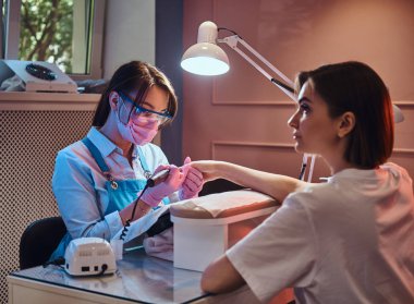 Genç manikür ustası işyerinde kadın tırnakları üzerinde çalışıyor..