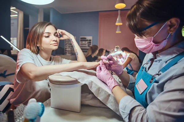 Atrakcyjna młoda kobieta z tatuażem jest coraz pielęgnacji paznokci z manicurist. — Zdjęcie stockowe