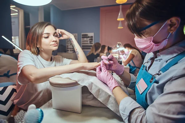 Atrakcyjna młoda kobieta z tatuażem jest coraz pielęgnacji paznokci z manicurist. — Zdjęcie stockowe