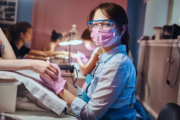 Joven maestra de manicura en su lugar de trabajo trabajando en uñas de mujer . — Foto de Stock