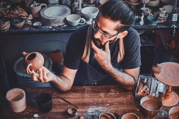 El hombre escéptico está mirando su propio trabajo, tetera de cerámica . — Foto de Stock