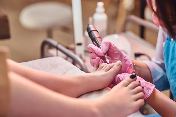 Young cheerful nail master is working on clients toe nails at her pedicure studio.