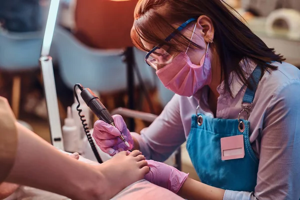 Młody wesoły mistrz paznokci jest praca na klientów paznokcie u nóg w jej studio pedicure. — Zdjęcie stockowe