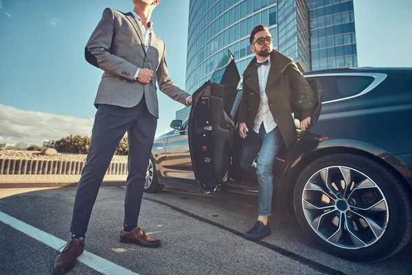 Inteligente empresario atractivo está saliendo del coche mientras que su asistente está abriendo la puerta para él . — Foto de Stock