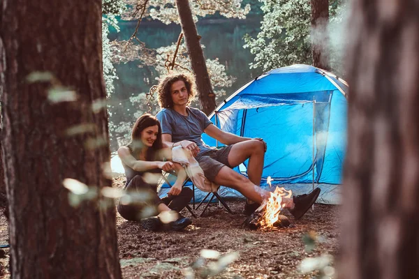 Attractive couple of young people chilling near bonfire in green sunny forest