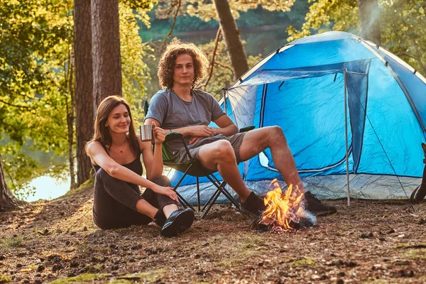 Attraktive junge Leute, die am Lagerfeuer im grünen, sonnigen Wald chillen — Stockfoto