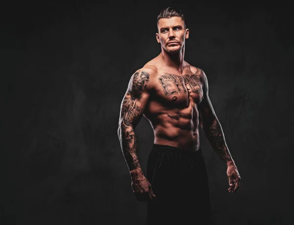 Un hombre musculoso tatuado sobre un fondo oscuro . — Foto de Stock