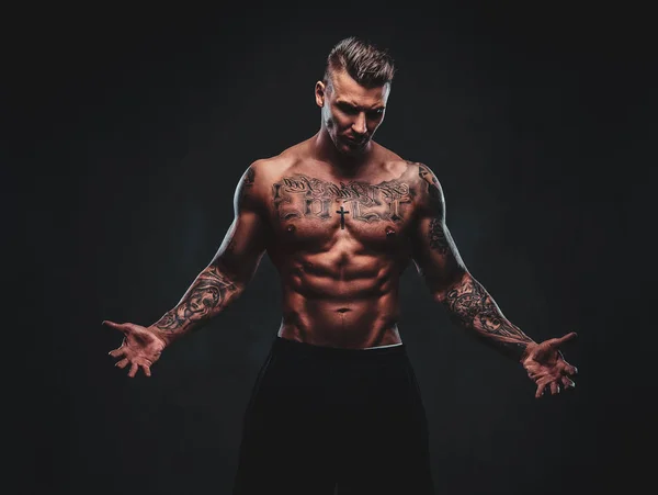 Un homme tatoué musclé sur un fond sombre . — Photo