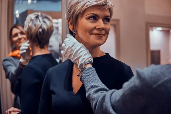 Mujer elegante se está probando hermosos pendientes con asistentes de tienda ayudan en la boutique de joyería de lujo —  Fotos de Stock