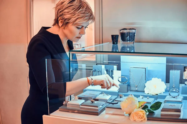 Shop Assistant zet nieuwe ornamentaties verscheidenheid van prachtige juweel tentoongesteld met bloemen in sieraden winkel — Stockfoto