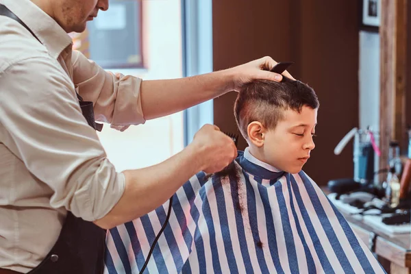 Menino da escola pequena teve seu primeiro corte de cabelo na moda na barbearia moderna . — Fotografia de Stock