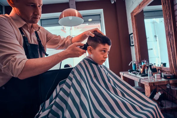 Симпатична маленька дитина отримує модну стрижку від перукаря в зайнятому перукарні — стокове фото