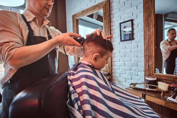 Cute little child is getting trendy haircut from barber at busy barbershop — Stock Photo, Image