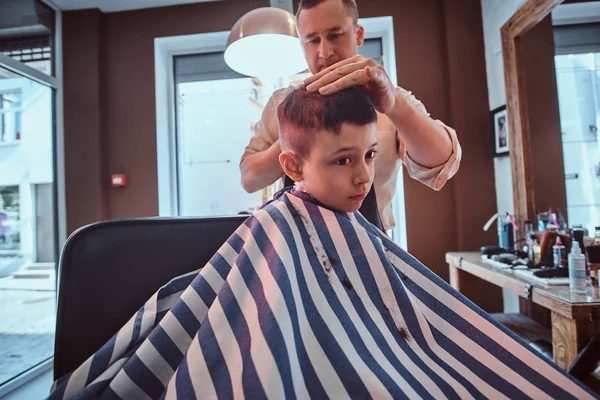 Cute little child is getting trendy haircut from barber at busy barbershop — Stock Photo, Image