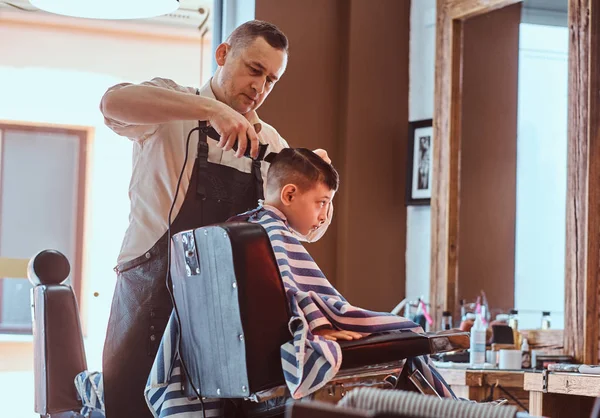 Menino da escola pequena está ficando moderno corte de cabelo de barbeiro expirienced na barbearia moderna — Fotografia de Stock