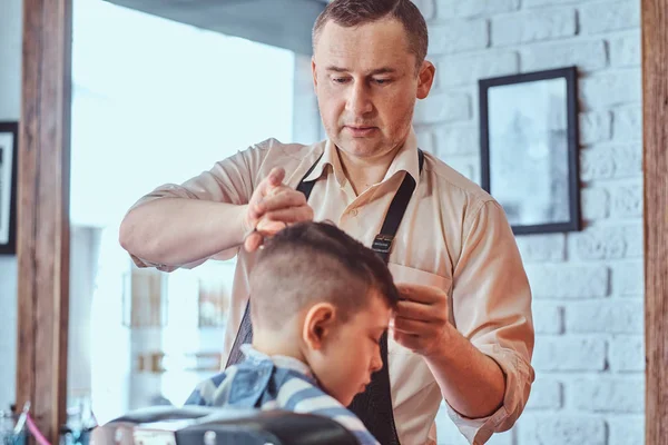 Menino da escola atraente está recebendo corte de cabelo na moda de cabeleireiro maduro no salão de cabeleireiro na moda — Fotografia de Stock