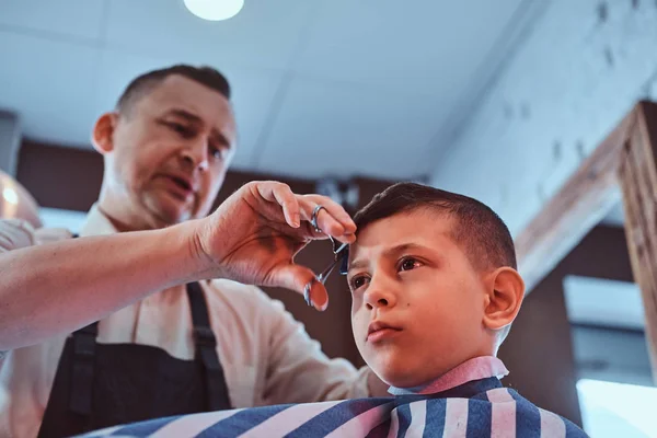 Attraktiv skol pojke blir trendiga frisyr från mogna frisör på fashionabla frisörsalong — Stockfoto