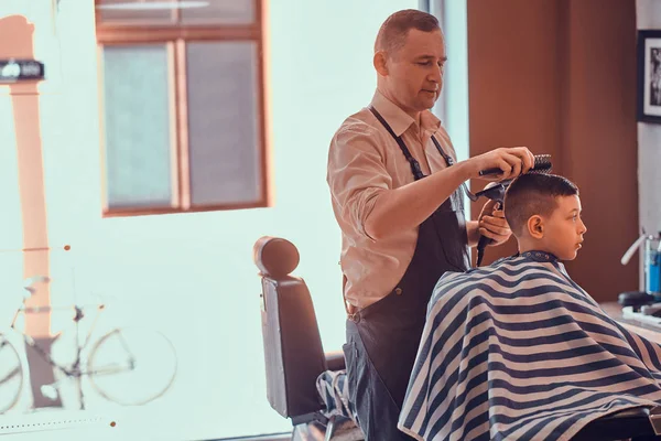 Engraçado menino está ficando moderno corte de cabelo de barbeiro expirienced na moda salão de cabeleireiro no firs tempo — Fotografia de Stock