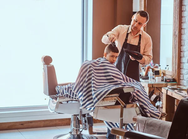 Engraçado menino está ficando moderno corte de cabelo de barbeiro expirienced na moda salão de cabeleireiro no firs tempo — Fotografia de Stock