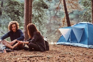 Genç mutlu öğrenciler yeşil ormanda şenlik ateşinin yanında ısınıyorlar.