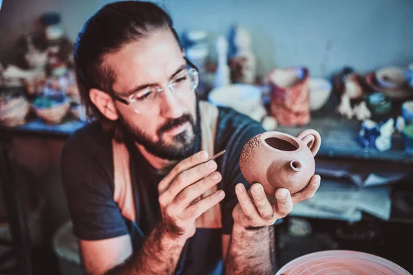 Pensive potter in glasses at his own workshop is workig on a new handmade teapot. — Stock Photo, Image